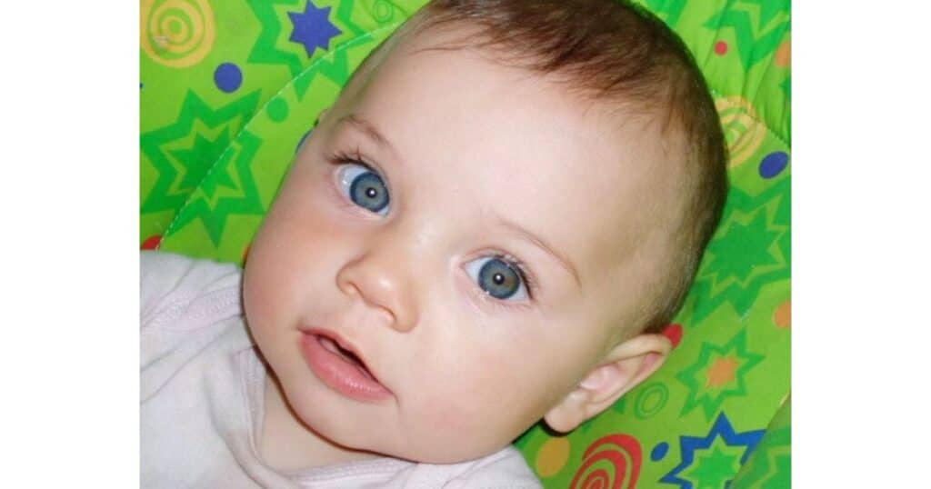 Development of oral language begins at birth. Close up of a baby's face on a green background with colorful shapes.