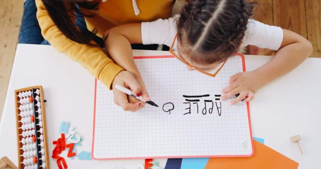 Mother helping child write words on a whiteboard. Create EBLI spelling word lists with your child from their own writing.