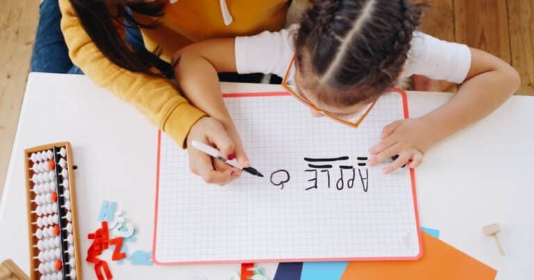 Mother helping child write words on a whiteboard. Create EBLI spelling word lists with your child from their own writing.