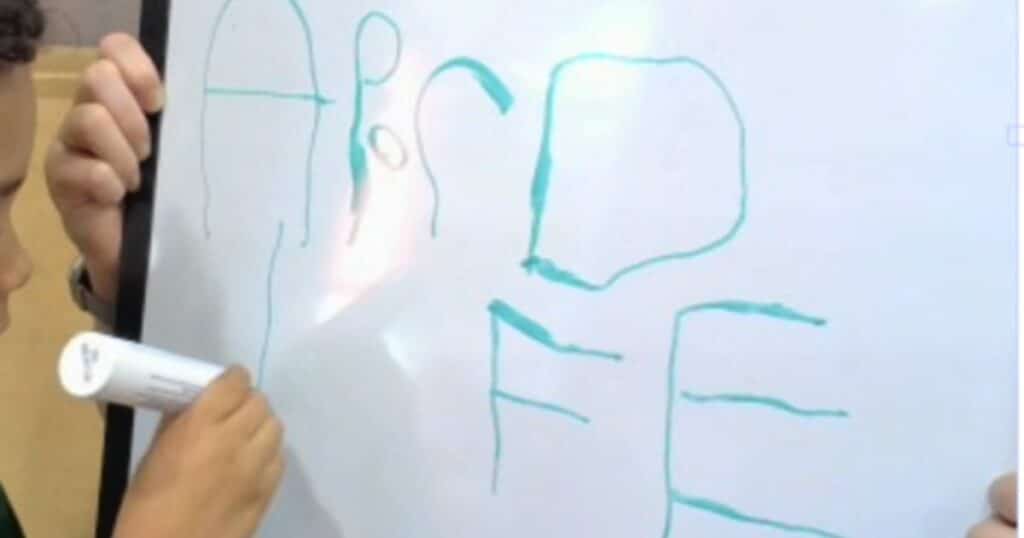Child writing the alphabet on a whiteboard. Writing in kindergarten means handwriting or letter formation.