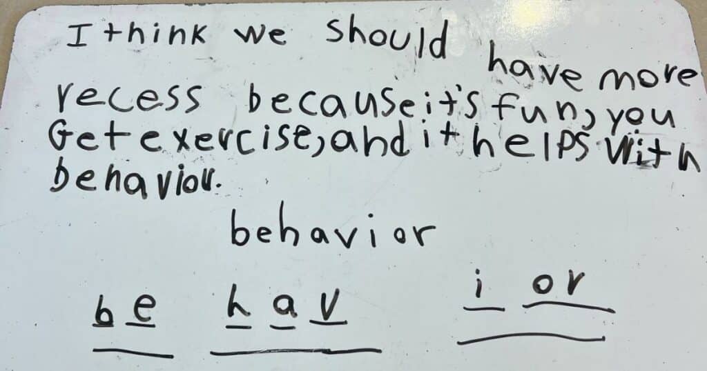 Student writing showing spelling corrections on a whiteboard with black marker.
